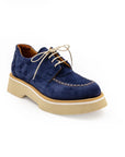 A blue suede shoe with a light-colored sole and lace-up closure, displayed against a white background.