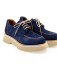 A blue suede shoe with a light-colored sole and lace-up closure, displayed against a white background.